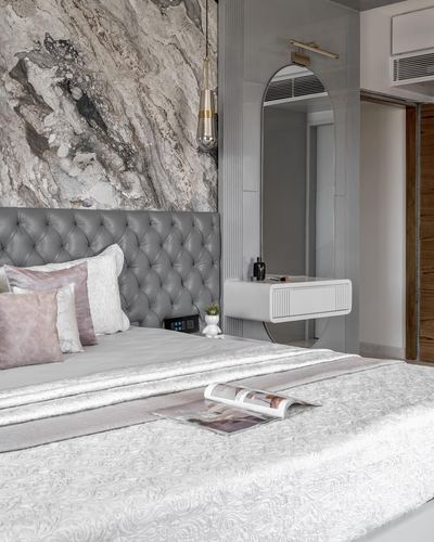Grey tufted bed against marble wall with arched mirror and floating vanity beside it