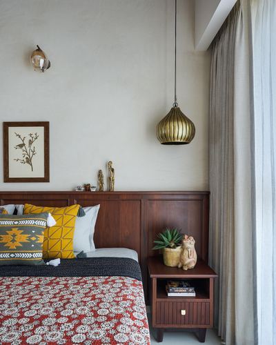 Bedroom corner with dark wood headboard, brass pendant light, and mustard patterned cushions