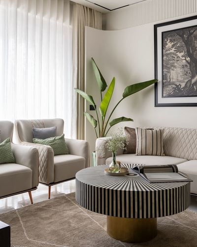 Neutral living room with quilted sofa, wing chairs, striped inlay coffee table, and large plant by window
