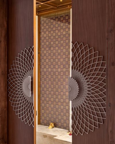 Two wooden doors with radial mandala cutwork open to a patterned pooja alcove with marble step
