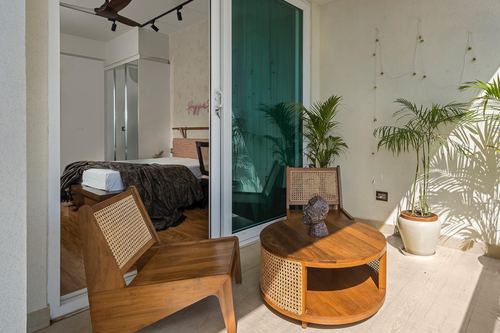 Balcony with cane armchair and round teak coffee table beside sliding glass door to bedroom