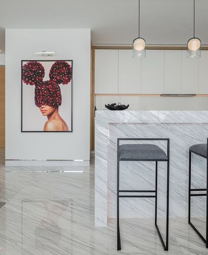 Modern kitchen with marble island, black stools, pendant lights and a floral portrait on the wall