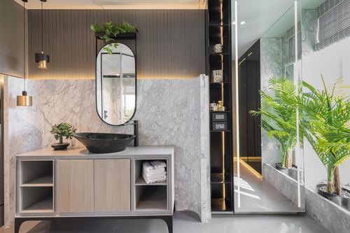 Bathroom vanity with black vessel sink, oval mirror, marble wall and wood cabinetry