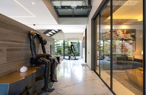 Marble-floored entry hallway with bronze sculptures, glass walls, and view into courtyard and living room