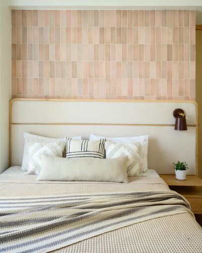 Bed with cream upholstered headboard against a pink vertical-tile wall, layered neutral pillows