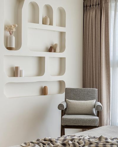 Sculpted arched wall niches with ceramic vases beside a grey boucle armchair in a beige bedroom