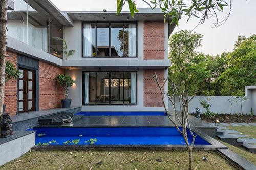 Two-storey brick and concrete home with large glazed windows overlooking a sunken blue swimming pool.