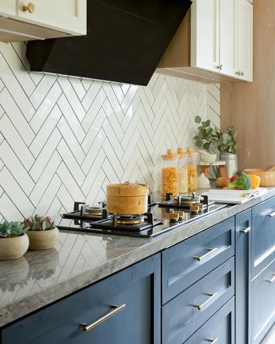 Navy kitchen counter with gas hob, herringbone tile backsplash and black range hood