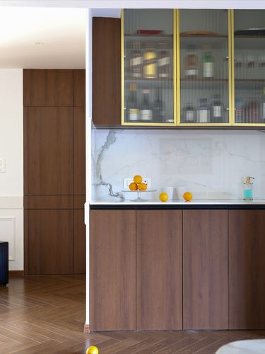 Walnut kitchen cabinetry with brass-fluted glass upper cabinets and marble backsplash, oranges on counter