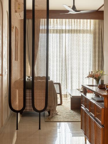 Cane room dividers frame a softly lit bedroom with sheer curtains and wooden sideboard