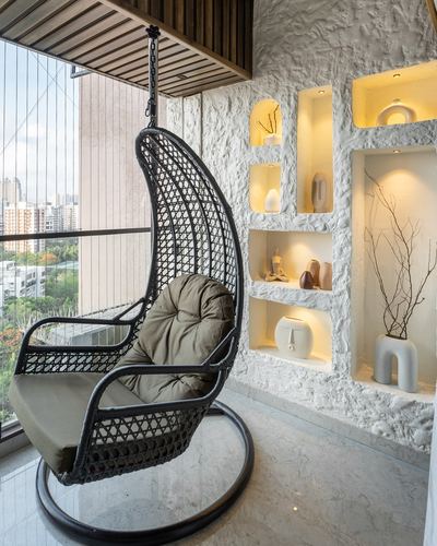 Black rattan hanging chair on marble balcony beside textured white niche wall with ceramics