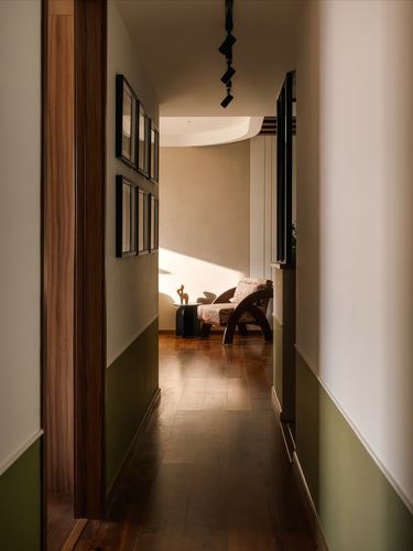 Wood-floored corridor with framed art leading to a sunlit curved armchair nook