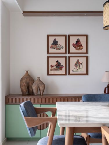 Dining nook with marble table, blue chairs, sage cabinet, and four framed folk portraits above.
