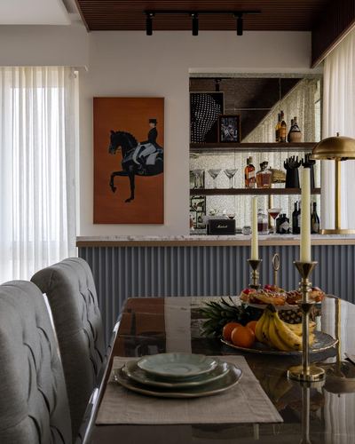 Dining table set with fruit and candlesticks beneath a bar niche and horse painting in a warm-toned room