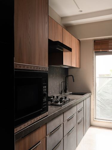 Galley kitchen with wood-veneer cabinets, dark stone counter, built-in microwave, and window with cane blind