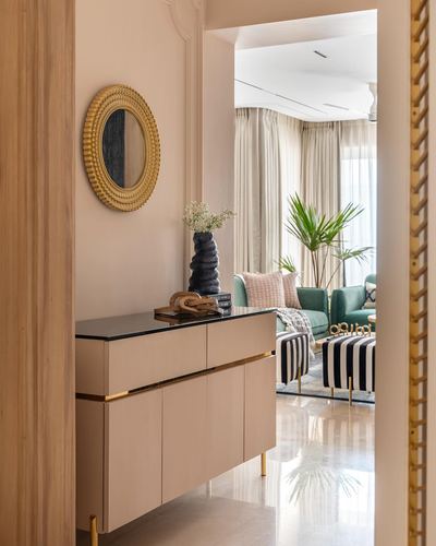 Pink foyer with round gold mirror and console table opening into a green-sofa living room