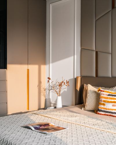 Sunlit bedroom corner with tufted leather headboard, pendant light, and dried branches in vase