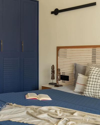 Bedroom corner with navy louvered wardrobe, striped woven headboard, and open book on bed