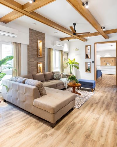 Living room with beige sectional sofa, crisscross wood ceiling beams, and stone-clad niche wall.