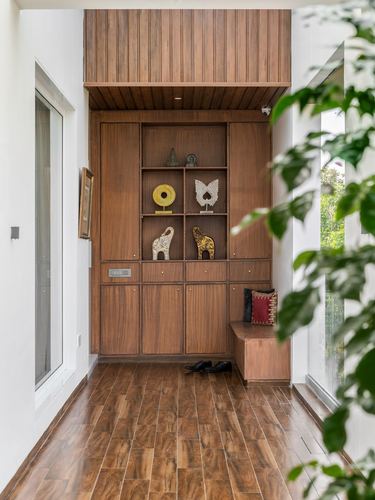 Wood-paneled foyer cabinet with display niches, bench, and wood flooring beside glass doors