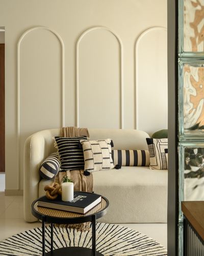 Cream sofa with patterned cushions against arched wall paneling, round cane table in front