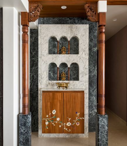 Pooja alcove with arched marble niches, carved wooden pillars, brass idols and inlay cabinet