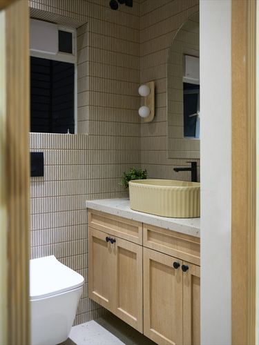 Bathroom vanity with ribbed yellow sink, wood cabinetry, and fluted tile walls, seen through arched doorway