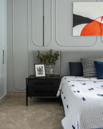 Grey panelled bedroom wall with velvet headboard, dark wood nightstand, and abstract art above bed