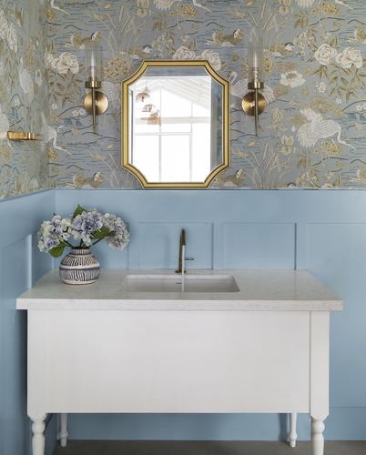 Powder room vanity with gold mirror, brass sconces, floral wallpaper and blue paneled wainscoting