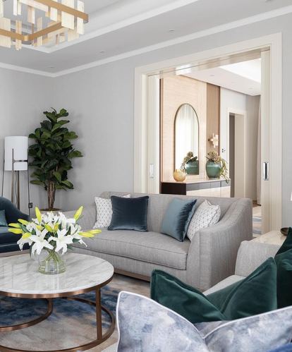 Gray sofa with teal velvet pillows around a round marble coffee table, chandelier above, arched mirror visible through doorway