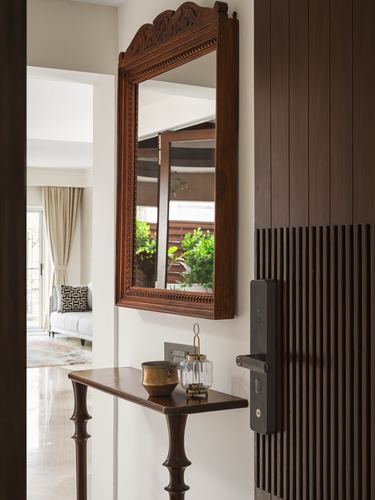 Foyer with carved wooden mirror above console table beside a fluted wood door
