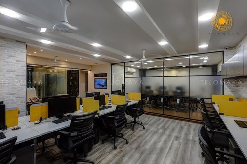 Open-plan office with white desks, black chairs, yellow partitions and glass-walled meeting room
