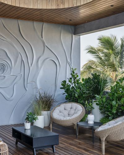Terrace with carved wave-pattern wall, cane chairs, and palm trees against sky