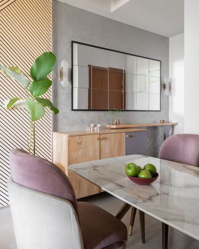 Dining nook with marble table, mauve velvet chairs, wood sideboard and paneled mirror on textured wall