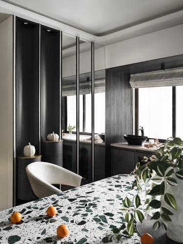 Dark wood kitchen counter with black vessel sink beside terrazzo island and mirrored storage panels