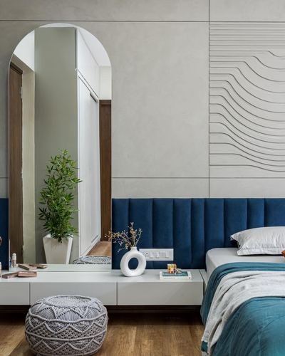 Bedroom corner with arched mirror, wavy fluted wall panel, and navy channel-tufted headboard
