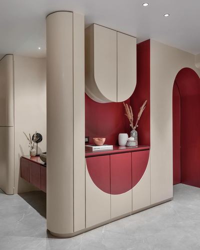 Curved beige cabinetry with arched maroon niche and styled console in a Mumbai foyer