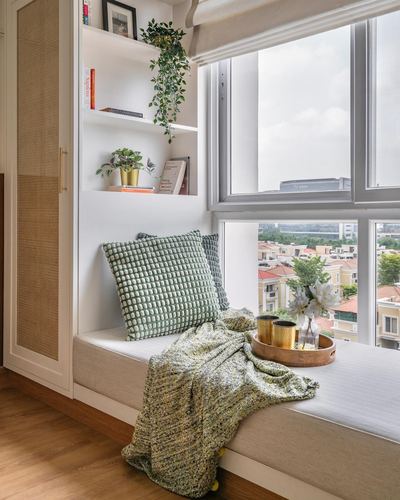 Window seat nook with green cushions, knit throw, and shelving overlooking a city skyline