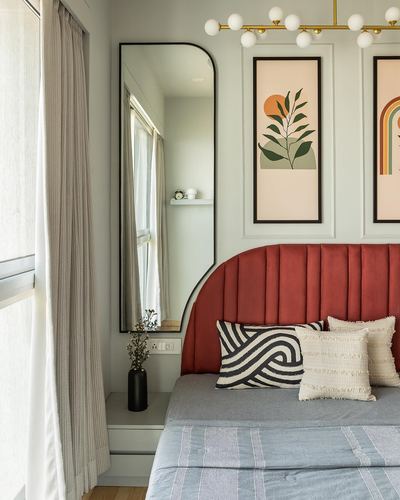 Bedroom corner with arched mirror, terracotta velvet headboard, and framed prints under a globe chandelier