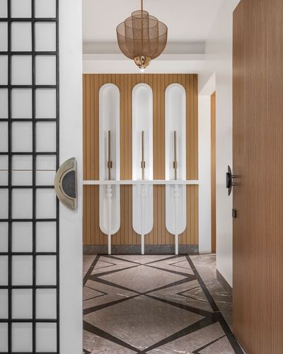 View through a black-grid glass door into a foyer with fluted wood wall, arched white panels, and patterned marble floor.