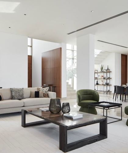 Open-plan living room with cream sofa, dark wood coffee table, olive velvet chair, and glass staircase beyond