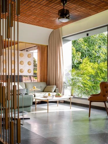 Living room with slatted wood ceiling, sage sofa, and glass wall opening to greenery