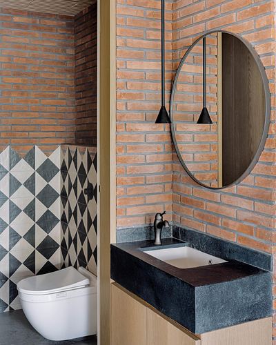Bathroom with exposed brick walls, round mirror, black pendant lights, and dark stone vanity