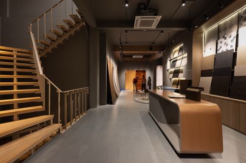 Showroom interior with wood staircase, curved counter and material sample wall under track lighting