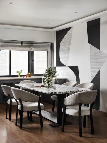 Dining table with patterned stone top and cane-back chairs beneath a bold black-and-white wall mural