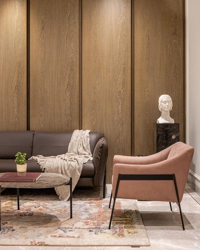 Living room with wood-paneled wall, brown leather sofa, pink armchair, and marble bust on pedestal