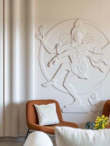 Sculpted Nataraja relief on fluted white wall behind a terracotta boucle armchair