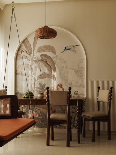 Dining nook with carved wooden chairs beneath an arched botanical mural and rattan pendant light