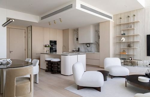 Open-plan cream kitchen and living area with marble backsplash and curved white chairs