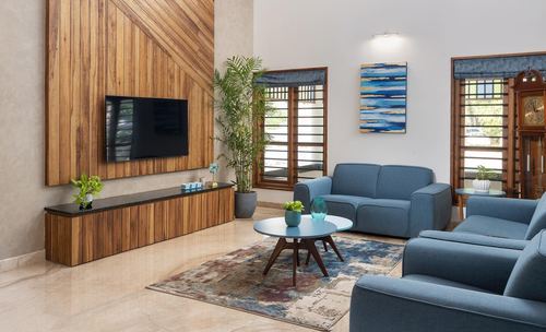 Living room with wood-paneled tv wall, blue sofas, round coffee table and marble floor